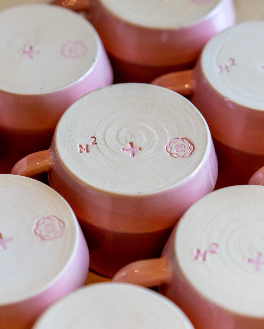 A group of pink mugs are arranged on a table at a Coffee Shop.