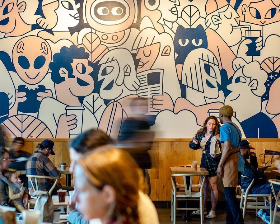 People are sitting at tables in a Coffee Shop with a mural on the wall.