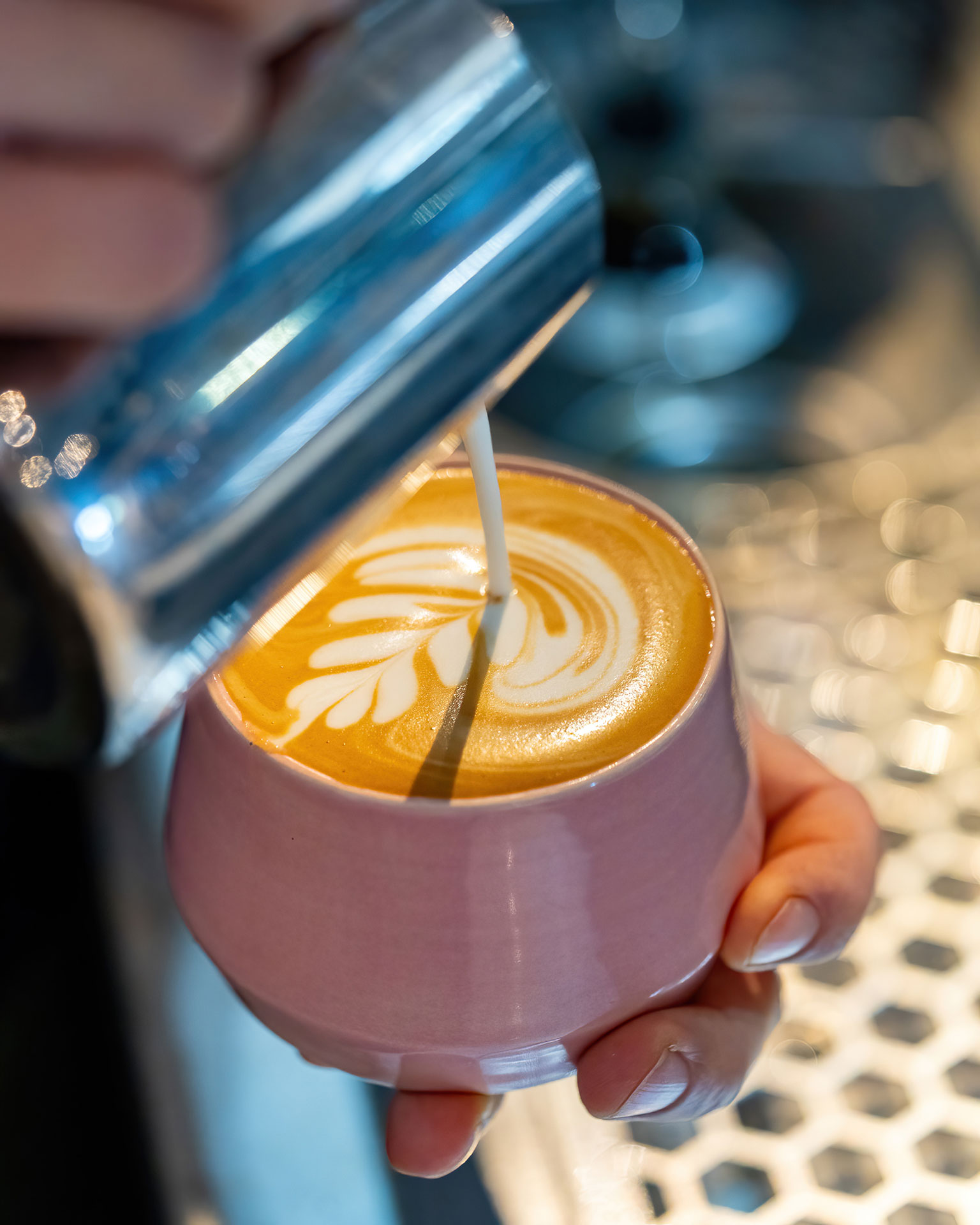 A person pouring latte into a pink cup at a Coffee Shop.